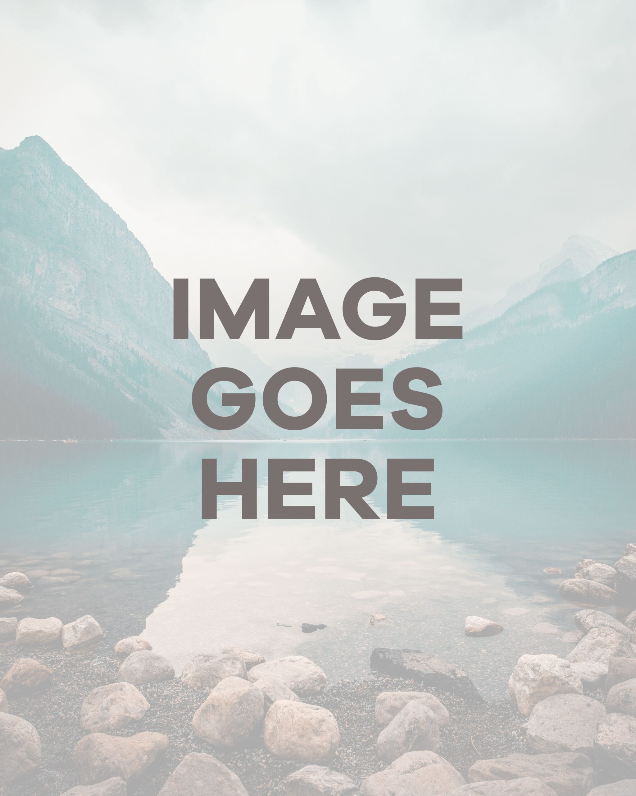 Misty mountain landscape with rocky shoreline and calm water, serene nature scene.