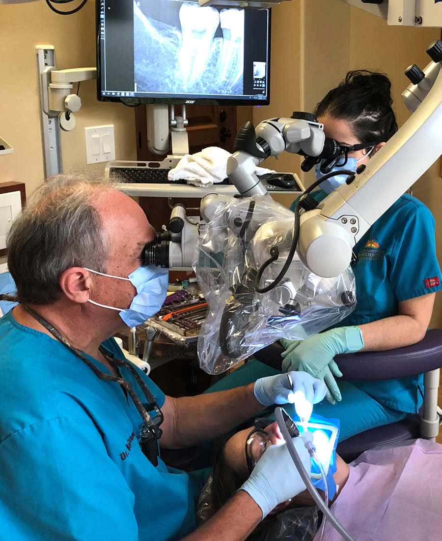 Two dental professionals performing endodontic procedure on patient in clinical treatment room.