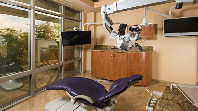 Modern dental operatory with blue chair, equipment, and large windows in contemporary clinic setting.
