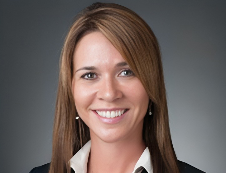 Professional headshot of a smiling woman in business attire against a gray background.