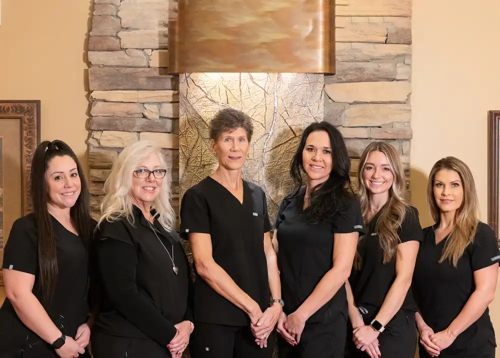 Six female dental professionals in black uniforms standing together in a modern dental office.